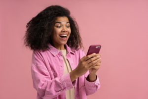 A woman dressed in pink, holding a pink phone. The woman is smiling at her phone. 